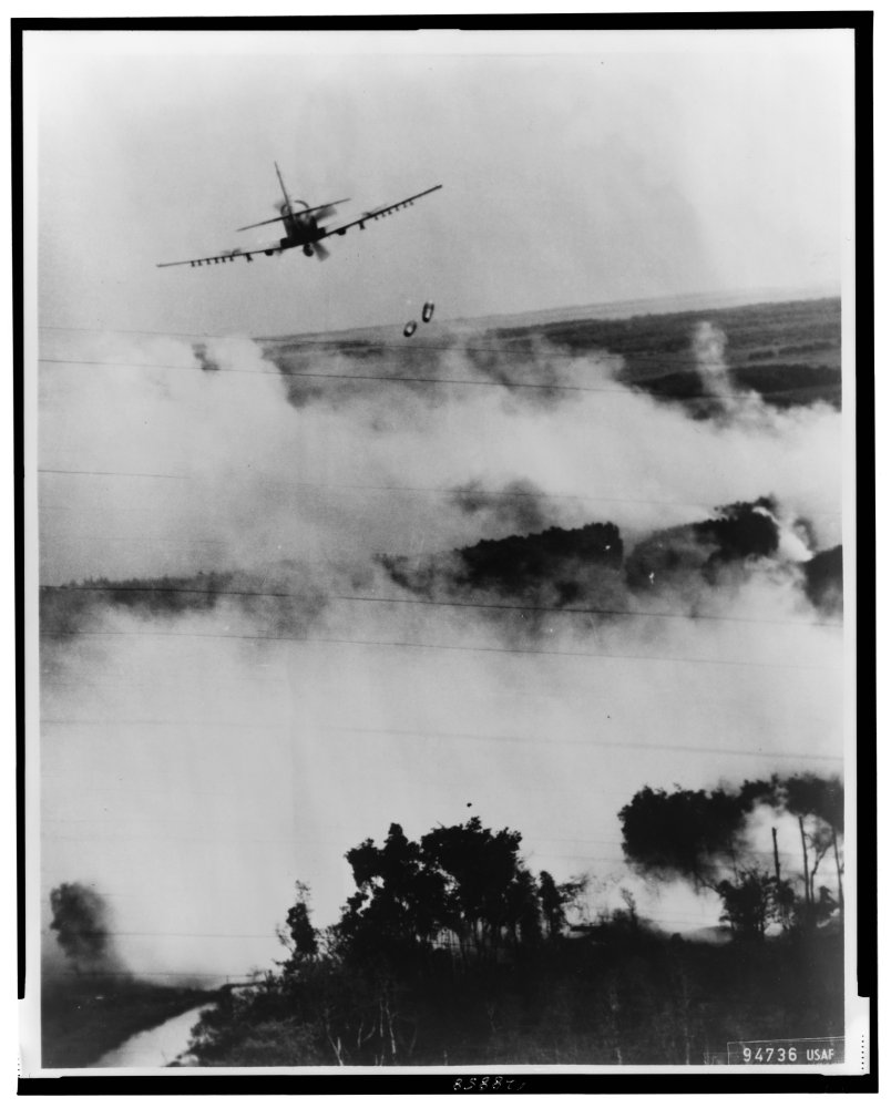 Two bombs tumble from a Vietnamese Air Force A - 1E Skyraider over a burning [Viet] Cong hideout near Cantho, South Viet Nam, 1967. Library of Congress, EUA.